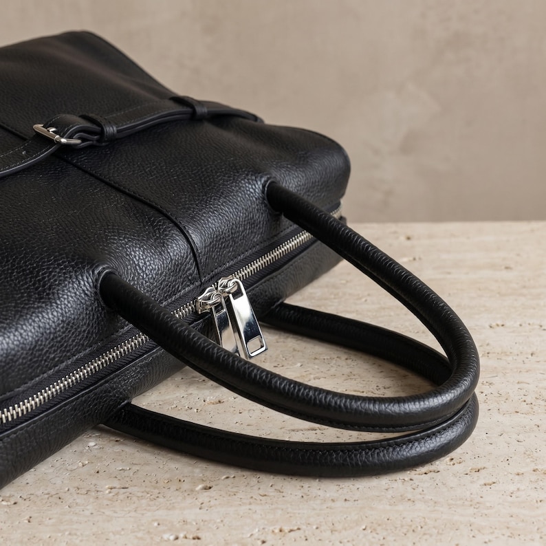 Detail of the twin rolled top handles and secure top zipper closure on the textured black leather office handbag, showcasing polished silver-tone hardware and clean stitching.