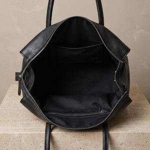 Interior of the large office handbag showing the fabric-lined compartment with one inner zip pocket and one open pocket, keeping work essentials organized in textured black leather.