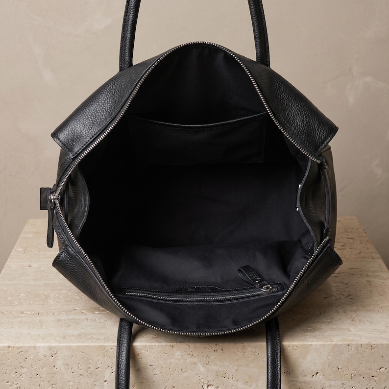 Interior of the large office handbag showing the fabric-lined compartment with one inner zip pocket and one open pocket, keeping work essentials organized in textured black leather.