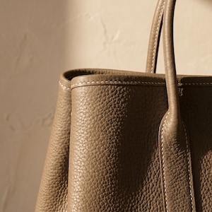 Close-up macro of the pebbled full grain cowhide leather and hand saddle-stitching on the khaki leather tote bag, highlighting premium texture and craftsmanship.
