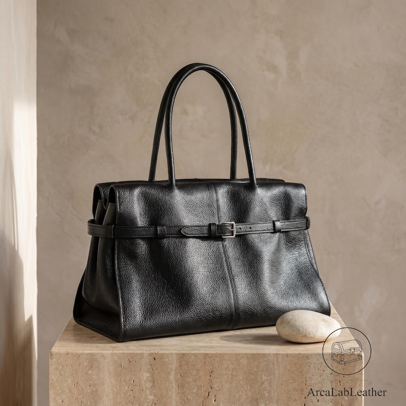Large office handbag in textured black genuine leather, a structured leather crossbody purse with twin rolled top handles, silver buckle front strap and adjustable shoulder strap, shown from the front.