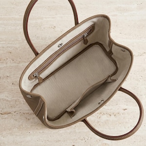 Top-down view inside the khaki leather tote bag showing the canvas-lined interior with zip pocket, phone slip pocket and roomy large-capacity main compartment.