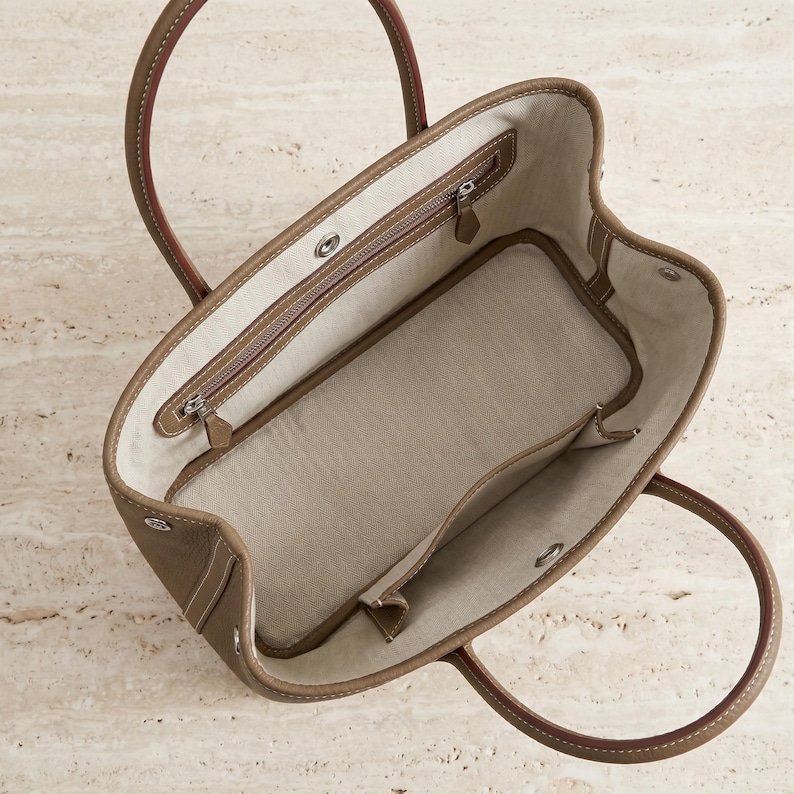 Top-down view inside the khaki leather tote bag showing the canvas-lined interior with zip pocket, phone slip pocket and roomy large-capacity main compartment.
