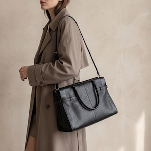 Lifestyle shot of the black leather office handbag worn crossbody with its adjustable strap, showing how the everyday genuine leather purse fits a hands-free workday commute.