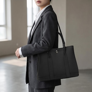 Woman wearing the black leather tote bag crossbody with the adjustable strap, showing the hands-free everyday carry of the full grain cowhide shoulder bag.
