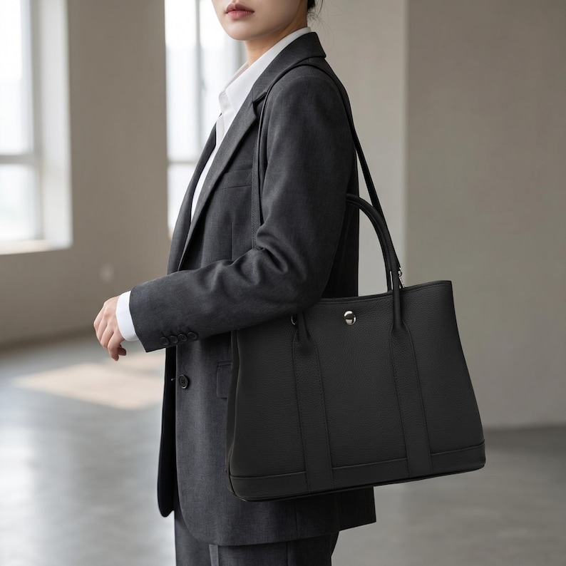 Woman wearing the black leather tote bag crossbody with the adjustable strap, showing the hands-free everyday carry of the full grain cowhide shoulder bag.