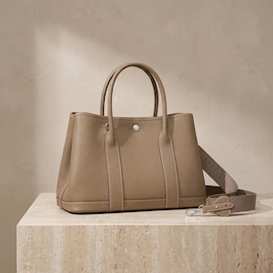 Side profile of the khaki leather tote bag showing the soft pleated gusset, flat base, side slip pocket and structured horizontal silhouette of the cowhide shoulder bag.