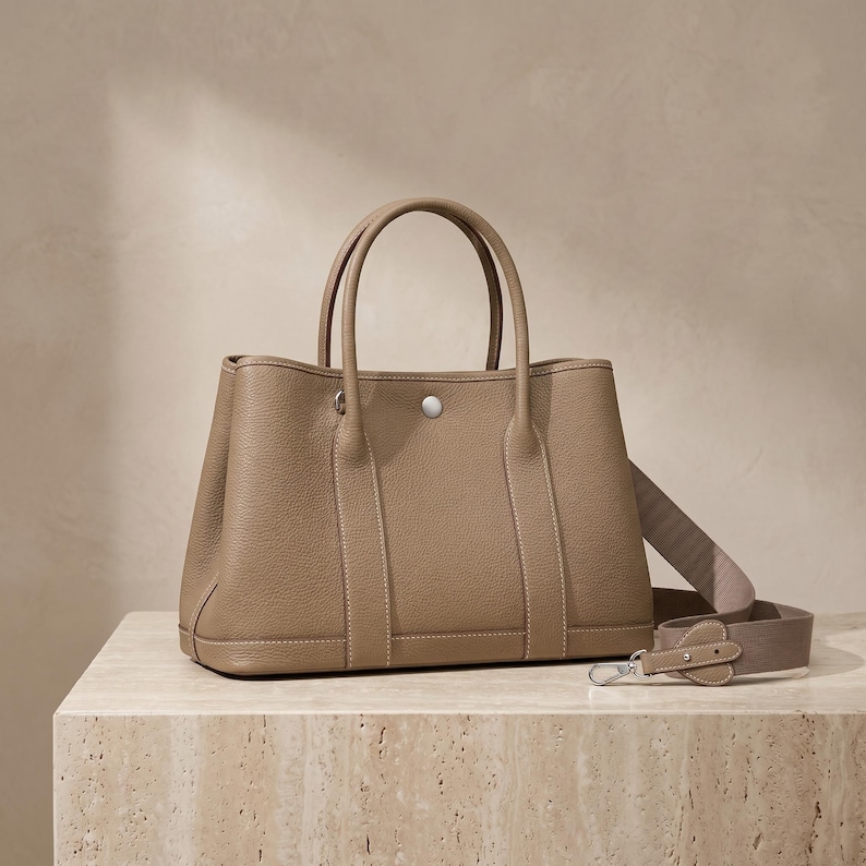 Side profile of the khaki leather tote bag showing the soft pleated gusset, flat base, side slip pocket and structured horizontal silhouette of the cowhide shoulder bag.