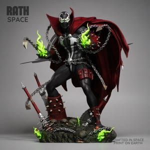 May include: A Spawn action figure statue featuring a black suit with white markings, a flowing red cape, and silver chains. The figure has green flames on its hands, spiked red boots, and stands on a rocky base with weapons. Text reads RATH SPACE.