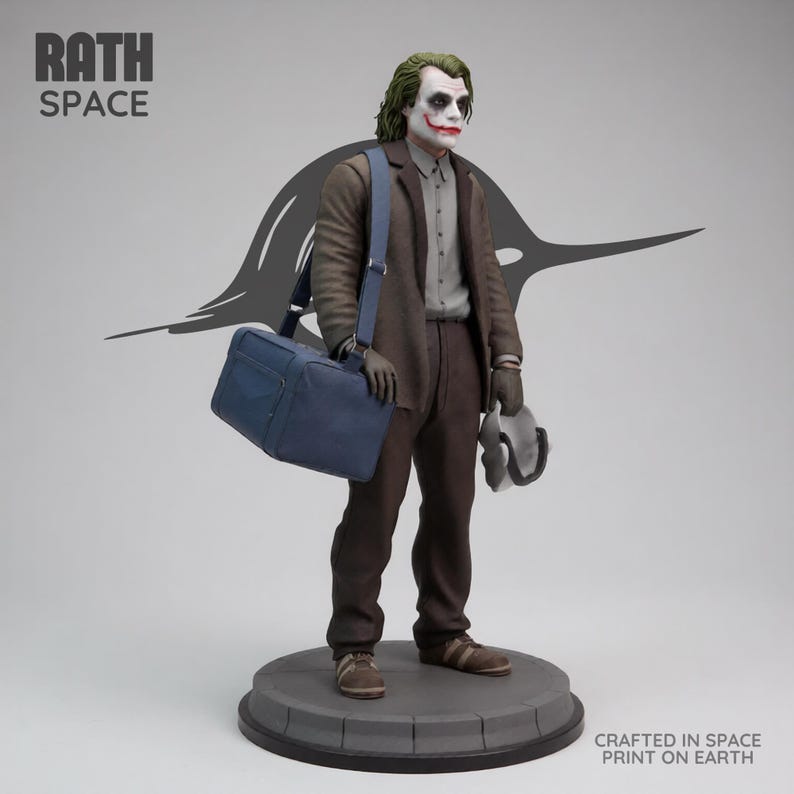 May include: A statue of the Joker character from the Batman franchise. The figure is wearing a brown suit, carrying a blue bag and a mask. The statue is on a gray circular base. The text "RATH SPACE" and "CRAFTED IN SPACE PRINT ON EARTH" are visible.