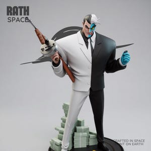 May include: A statue of the DC Comics villain Two-Face, split down the middle with a white and black suit. He holds a Tommy gun and stands on a base with stacks of money. The statue has the text "RATH SPACE" and "CRAFTED IN SPACE PRINT ON EARTH".