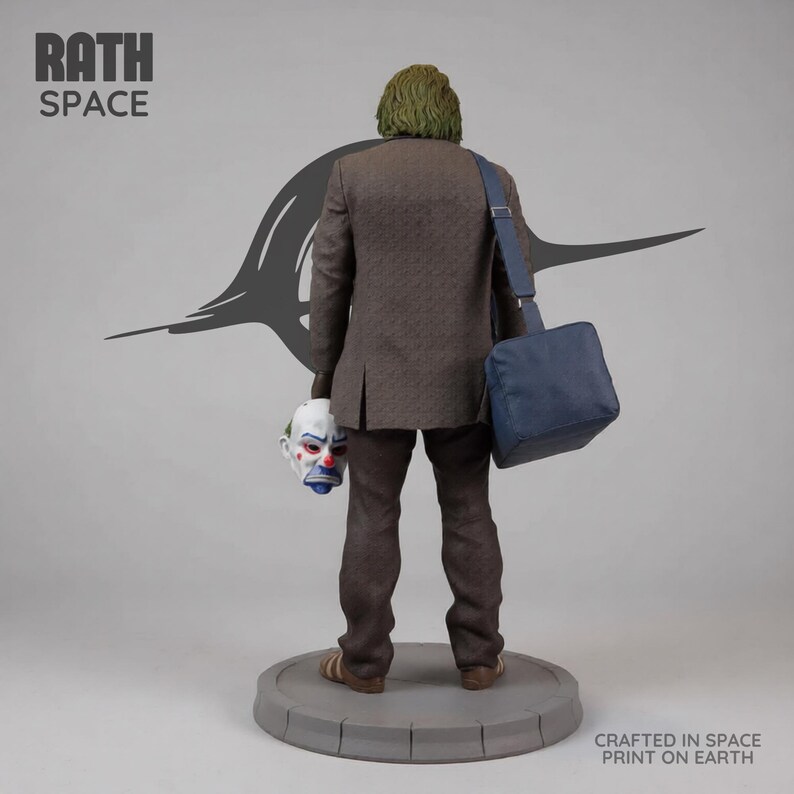 May include: A statue of a figure in a brown suit, holding a clown mask and a blue bag. The figure has green hair and is standing on a gray circular base. The text "RATH SPACE" is at the top left. The text "CRAFTED IN SPACE PRINT ON EARTH" is at the bottom right.
