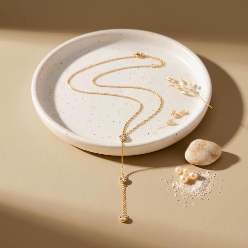 May include: A gold-toned lariat necklace featuring a delicate chain and three evenly spaced round clear stones set in gold-toned metal. The necklace is arranged in a Y-shape, with the chain extending downward from the top stone to the bottom.