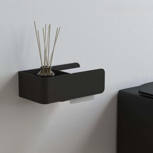 May include: A matte black wall-mounted bathroom shelf featuring a rectangular storage compartment and an integrated toilet roll holder. A small glass diffuser bottle with thin wooden reeds sits inside the storage section of the shelf.