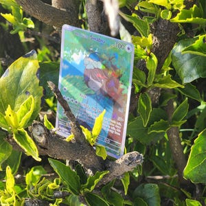 May include: A holographic Pokemon trading card featuring Swablu, a blue and white bird Pokemon. The card has a blue background with a picture of Swablu in the center. The card's name, Swablu, is printed in white letters at the top of the card. The card's number, 100, is printed in white letters at the top right corner of the card. The card's attack, "Puff Up The Jam", is printed in purple letters at the bottom of the card.