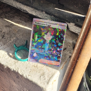 May include: A holographic Pokemon trading card featuring a character named Philomena Cunk. The card is a Trainer card and has a blue, green, and purple color scheme. The card text reads "You may play only 1 Supporter card during your turn."