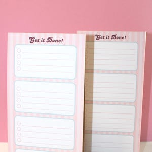 May include: Two vertical paper notepads with a light pink and white striped background. Each notepad features the text "Get it Done!" at the top, followed by four rectangular sections, each containing four circular checkboxes and horizontal lines.