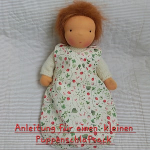 May include: A handmade doll with red hair and a neutral skin tone, wearing a white dress with a floral pattern of red berries and green leaves. The doll's arms and legs are a light orange color. The text at the bottom reads "Anleitung für einen kleinen Puppenschlafsack."