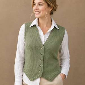 May include: A sage green knitted vest featuring a V-neckline and a front button closure with five matching buttons. The sleeveless garment has a ribbed texture and a pointed hemline, worn over a white long-sleeved shirt with thin vertical stripes.