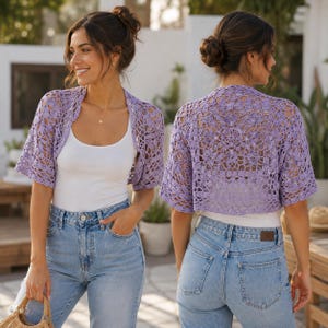 May include: A light purple crochet bolero featuring an intricate openwork floral pattern with short sleeves and a cropped silhouette, worn over a plain white tank top and light blue denim jeans, shown from both the front and back perspectives.