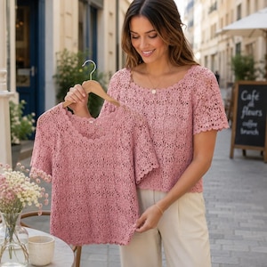 May include: A dusty rose short-sleeved top featuring an intricate openwork crochet pattern with a scalloped neckline and hem. The garment is constructed from a lightweight knit fabric with a repeating floral-inspired design throughout the body.