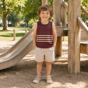 May include: A sleeveless maroon knit tank top featuring three horizontal cream-colored stripes across the chest, paired with light beige shorts and matching beige sneakers with hook-and-loop closures, worn by a young child with curly brown hair.