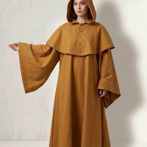 May include: A floor-length, mustard-yellow hooded robe featuring wide, flared sleeves and a short, button-down capelet overlay that covers the shoulders. The garment is constructed with a solid-colored fabric and has a structured hood.