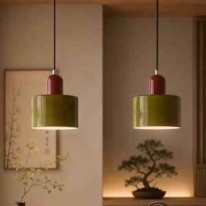 May include: Two cylindrical pendant lights featuring a glossy olive green shade and a smooth, rounded dark red top cap. Each lamp is suspended by a thin black cord, with a white interior finish that emits a soft, downward-facing light.