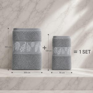 Peut inclure: Un ensemble de deux serviettes grises avec un motif botanique blanc. La plus grande serviette mesure 150 cm sur 100 cm et la plus petite mesure 130 cm sur 70 cm. Le texte 1 SET est affiché à droite des serviettes pour indiquer le lot.