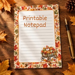 May include: A rectangular notepad featuring horizontal lines and the text Printable Notepad in orange. The border is decorated with autumn leaves, berries, and acorns. A small illustration of a wooden cart filled with pumpkins sits in the corner.