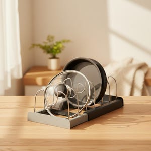May include: A black and silver adjustable kitchen organizer rack featuring vertical wire dividers. The rack holds a dark gray circular pan and a clear glass lid with a black knob, providing a structured storage solution for cookware.