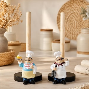 May include: Two vertical paper towel holders featuring chef figurines at the base. One chef wears a blue shirt with a red checkered scarf and holds a small cake. The other chef wears a white uniform with a red scarf and holds a black spoon.