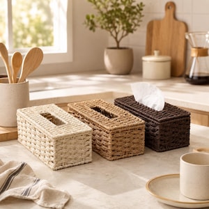 May include: Three rectangular tissue box covers made of woven material in cream, light brown, and dark brown. Each cover features a central rectangular opening on the top for dispensing tissues, with one box showing a white tissue protruding from it.