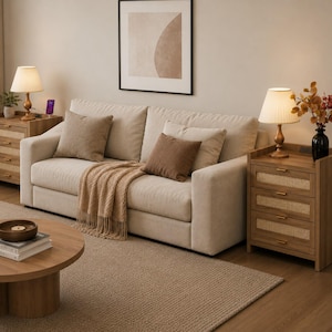 May include: A beige sofa with two brown throw pillows and a beige knit throw blanket, flanked by two wooden nightstands with three drawers featuring rattan panels, each topped with a lamp, and a round wooden coffee table in the foreground.