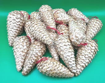 May include: A collection of multiple pine cone ornaments crafted from light beige, woven material. Each individual pine cone features a textured, layered scale pattern and is topped with a thin, red string loop for hanging purposes.
