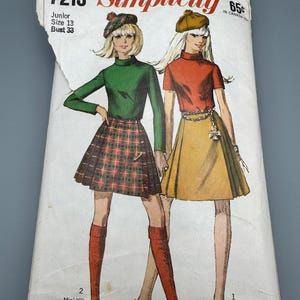 Puede incluir: Un sobre de patrón de costura vintage Simplicity 7213 para talla junior 13 con un busto de 84 cm. La ilustración muestra dos conjuntos: uno con una blusa verde de manga larga y minifalda de cuadros, y otro con una blusa roja de manga corta y falda amarilla.