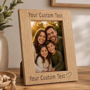 May include: A rectangular light-coloured wooden picture frame with a visible grain pattern. The top and bottom borders feature the engraved text "Your Custom Text" with a small heart symbol at the end of the bottom line, framing a family photo.