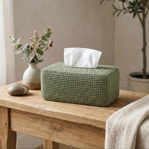 May include: A rectangular sage green crochet tissue box cover with a textured stitch pattern. A white tissue is pulled through the top opening. The text CROCHET TISSUE BOX, INSTANT DOWNLOAD, HIGH QUALITY, and PATTERN NO. 001 are visible.