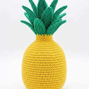 May include: A crochet pineapple toy featuring a rounded yellow body with a textured stitch pattern and a crown of pointed green leaves extending from the top. The object is crafted with yarn and displays a consistent, handmade appearance throughout.