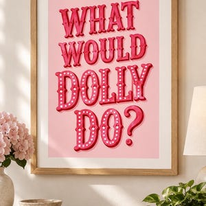 May include: A framed wall art print featuring a light pink background with the text WHAT WOULD DOLLY DO? in bold, dark pink, three-dimensional letters decorated with small white dots, encased in a simple light-coloured wooden frame.
