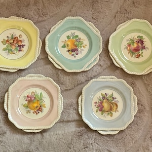 May include: A set of five octagonal ceramic plates with scalloped, rope-textured edges. Each plate features a unique pastel border in yellow, mint green, light green, pale pink, or light blue, with a central illustration of assorted fruits.