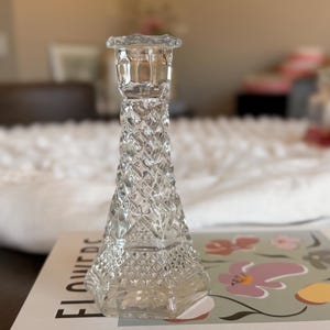May include: A clear glass candlestick holder featuring a textured diamond pattern across its tapered body. The piece has a flared base and a scalloped rim at the top, designed to hold a single taper candle securely in an upright position.