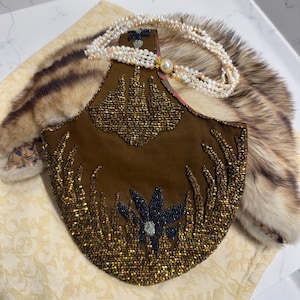May include: A brown fabric handbag featuring intricate gold and bronze beadwork in a floral and grass-like pattern, accompanied by a multi-strand white pearl necklace with a central pearl clasp, resting atop a brown and white striped fur accessory.