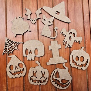 Op de afbeelding: Een set van 11 houten Halloween-uitsparingen, waaronder een heksenhoed, een spook, een schedel, een spinnenweb, een ketel, een vleermuis, een kat, een grafsteen en drie pompoenen. De uitsparingen zijn allemaal bruin en hebben een rustieke, handgemaakte uitstraling.