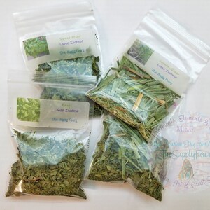 May include: Four small clear plastic bags filled with dried herbs labeled with the names of the herbs: Sweet Mint, Basil, Lemon Grass, and Lemon Grass. The bags are on a white surface. The text on the labels reads "Loose Incense" and "The Supply Faery".