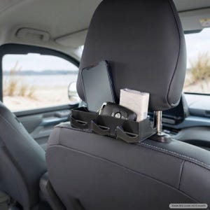 Puede incluir: Un organizador de asiento de coche de plástico negro montado en los postes del reposacabezas. El organizador cuenta con un compartimento rectangular que sostiene un teléfono inteligente y un paquete de pañuelos, además de una llave de coche.