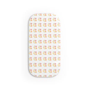 Pode incluir: Um lençol retangular para berço com um padrão repetitivo de pequenas flores de cinco pétalas em tons de rosa suave, amarelo e laranja sobre um fundo branco. O design floral está disposto em uma grade sobre a superfície do tecido.