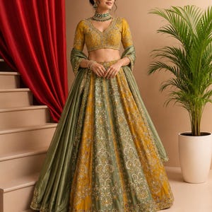 May include: A mustard yellow and olive green lehenga choli set featuring intricate silver embroidery, sequin work, and mirror embellishments. The ensemble includes a V-neck blouse with three-quarter sleeves and a matching dupatta draped over the arms.