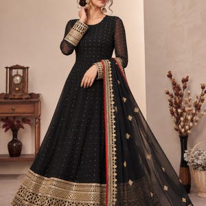 Könnte beinhalten: Ein bodenlanges, schwarzes Anarkali-Kleid mit langen Ärmeln, Rundhalsausschnitt und durchgehenden goldenen Paillettenverzierungen. Der Saum und die Ärmelbündchen sind mit aufwendigen Goldstickereien und Bogenkanten versehen, dazu ein passender Dupatta.