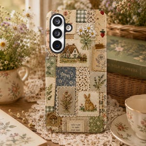 May include: A phone case featuring a patchwork design of embroidered fabric squares. The pattern includes a cottage, a rabbit, daisies, a mushroom, and a strawberry. The text "take time to make your soul" is printed on a small rectangular patch.